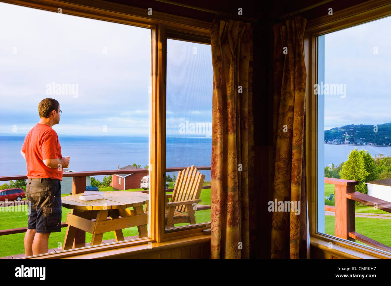 Uomo con una mattina tazza di caffè guardando sul fiume San Lorenzo a Cap-a-L'Aigle vicino a La Malbaie, Charlevoix, Québec Foto Stock