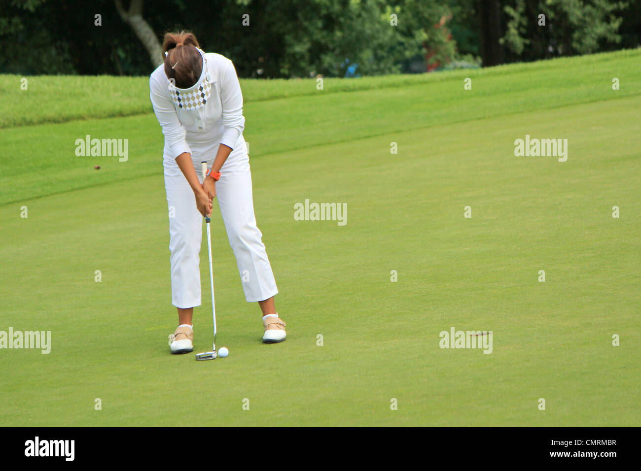 Donna golfista bianco da indossare i panni di golf, concentrando per mettere la palla sul foro sul verde Foto Stock