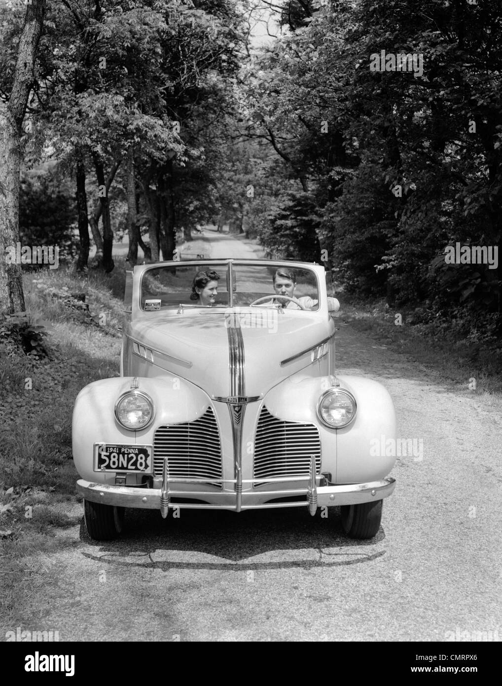 1940s 1941 GIOVANE UOMO E DONNA IN PONTIAC CONVERTIBLE guida su Vicolo del paese in campagna Foto Stock