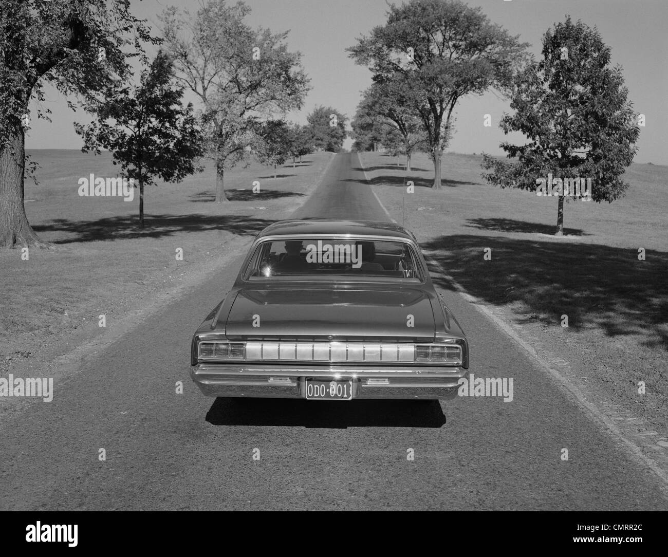 Anni sessanta VISTA POSTERIORE AUTOMOBILE la guida verso il basso COUNTRY ROAD Foto Stock