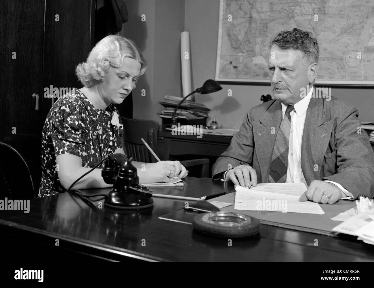 1930s 1940s imprenditore seduto alla scrivania di andare oltre la documentazione con il segretario sotto dettatura UOMO DONNA OFFICE INDOOR Foto Stock