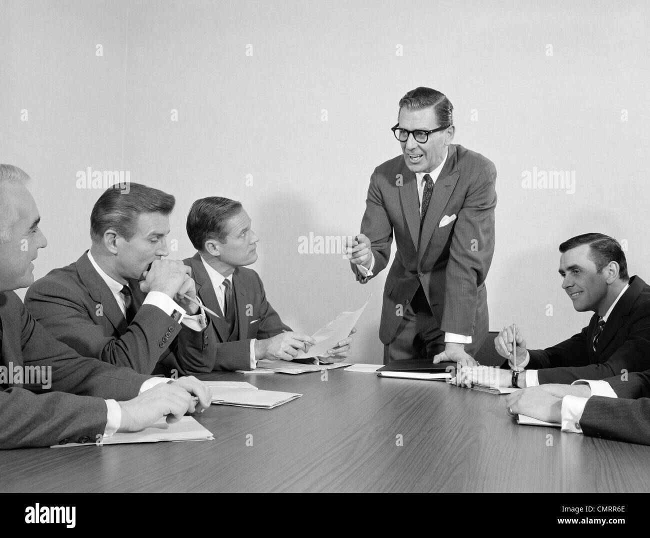 Anni sessanta 5 executive imprenditori riuniti a tavola per conferenze di un uomo in piedi Foto Stock