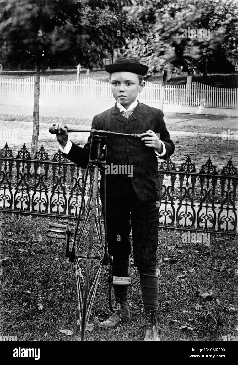 1800s 1890 1900s svolta del secolo BOY IN PIEDI IN CANTIERE ACCANTO ALLA VECCHIA BICICLETTA Foto Stock