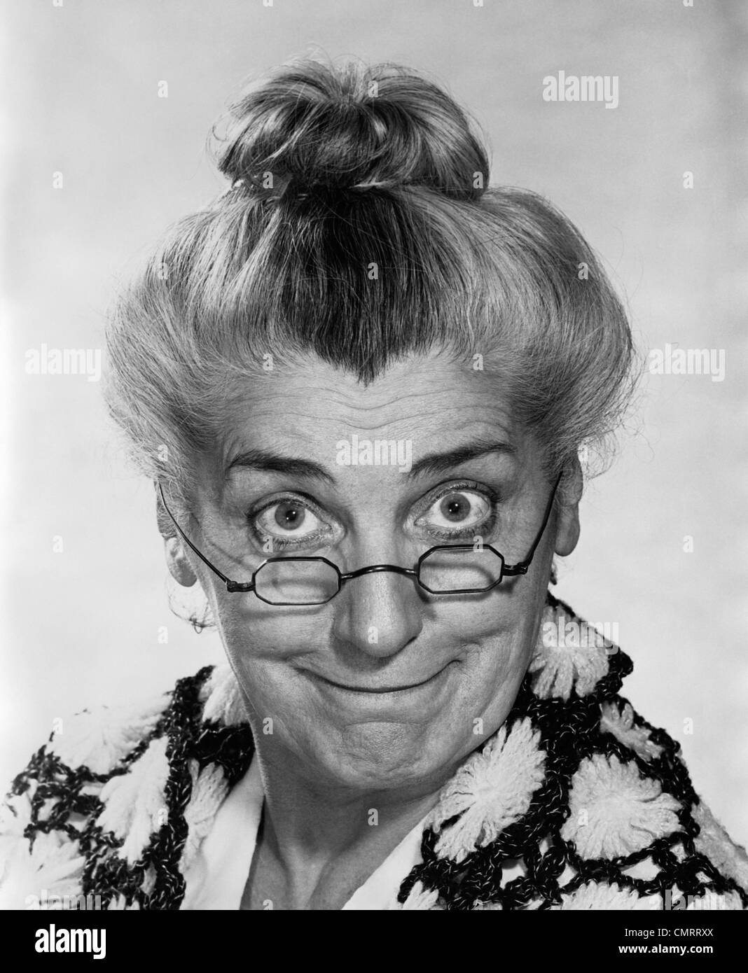 Anni Settanta anziani ritratto di donna con i capelli di BUN indossando occhiali da nonna sorridente guardando la fotocamera Foto Stock