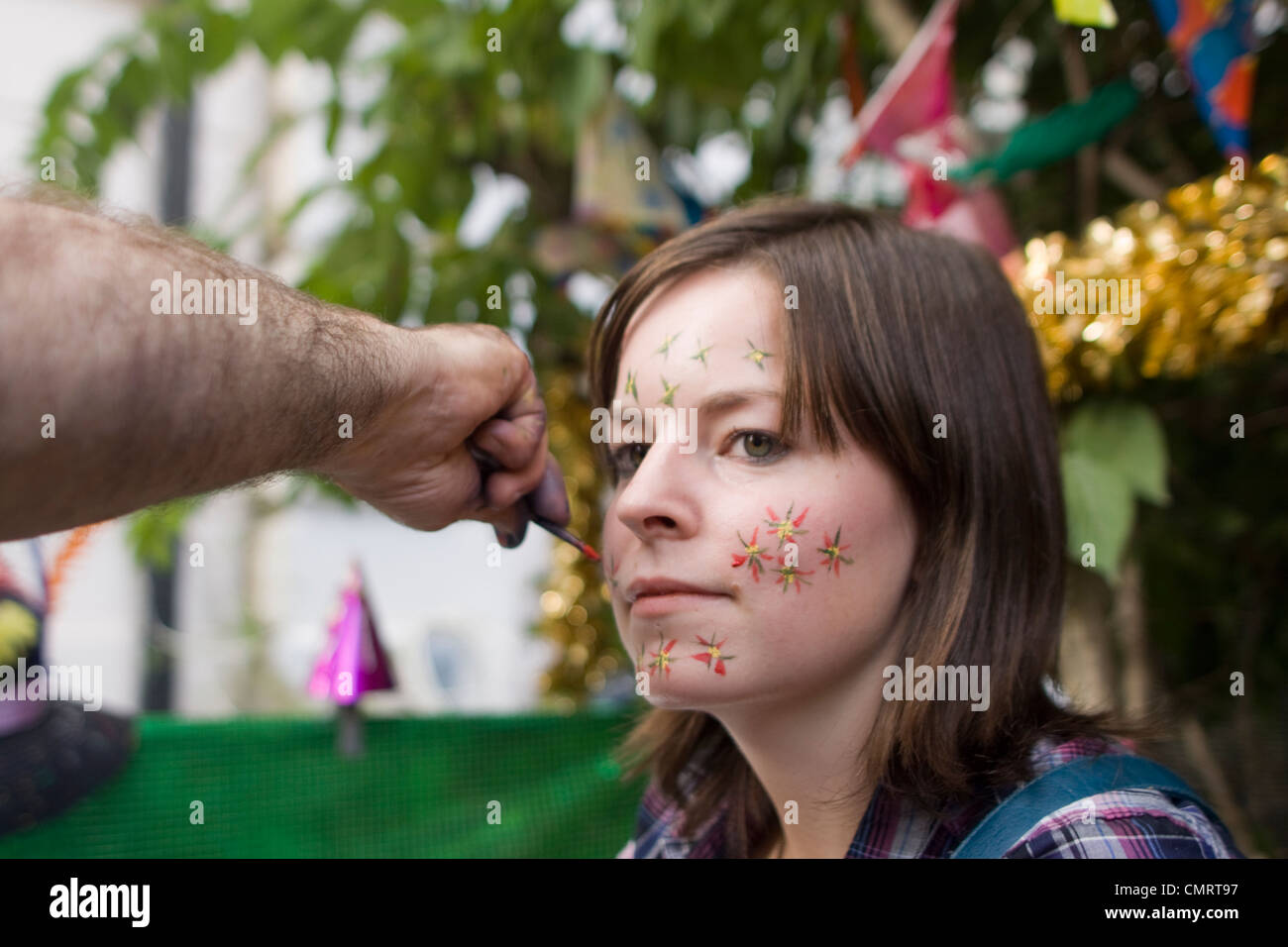 Un reveler al carnevale di Notting Hill a Londra ottenendo il suo volto dipinto. Foto Stock