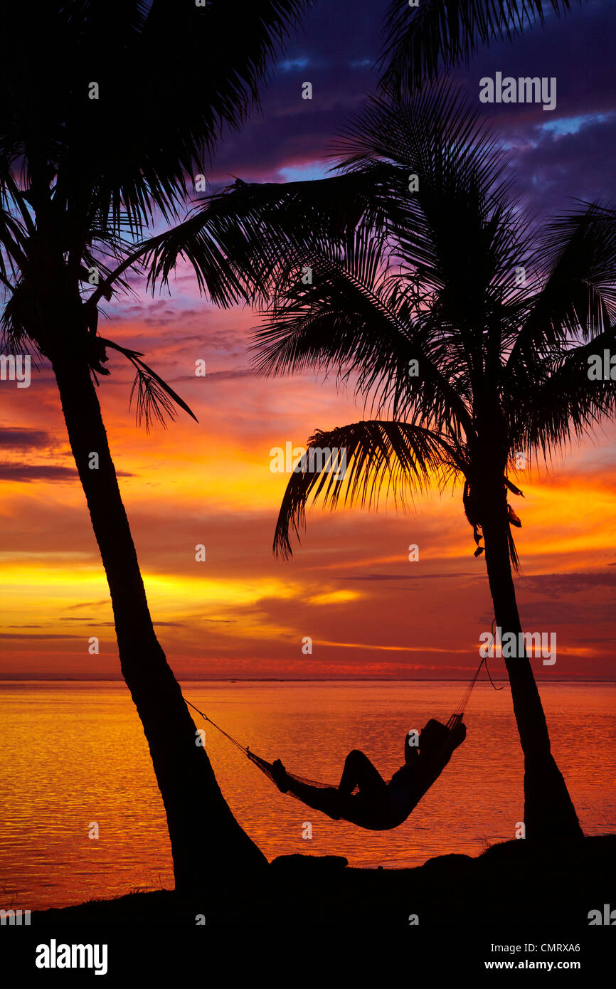 Donna in amaca e palme al tramonto, il litorale di corallo, Viti Levu, Figi e Sud Pacifico Foto Stock