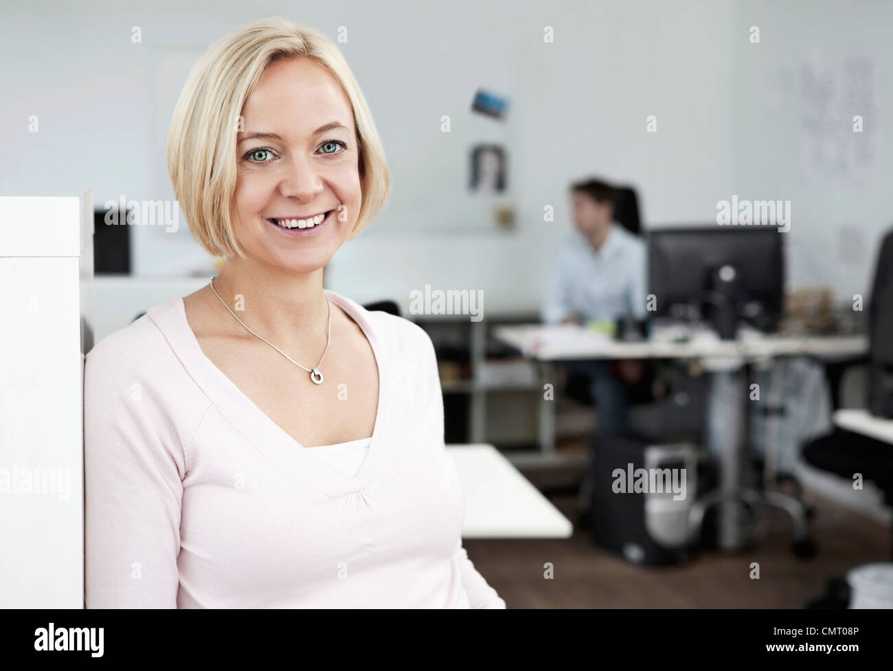 Donna sorridente in ufficio con le persone in background Foto Stock