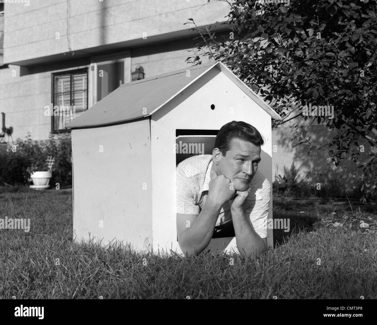 Anni sessanta l uomo nella cuccia nel cortile posteriore in appoggio sul  gomito a gomito con un cipiglio sul viso Foto stock - Alamy