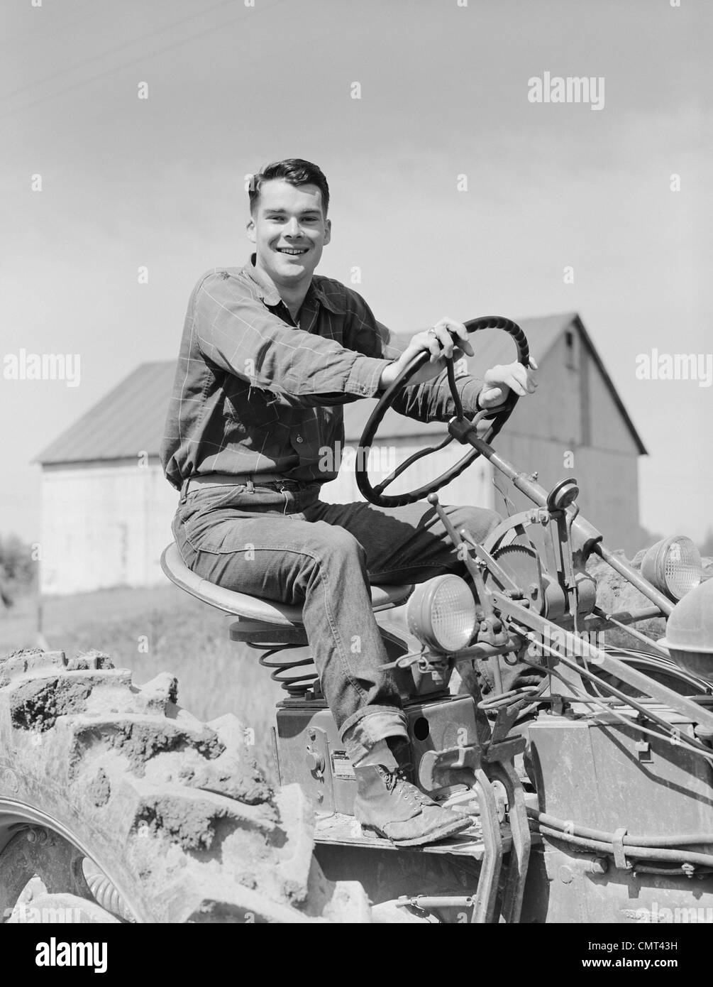 Anni Cinquanta uomo sorridente agricoltore la guida del trattore guardando la fotocamera Foto Stock