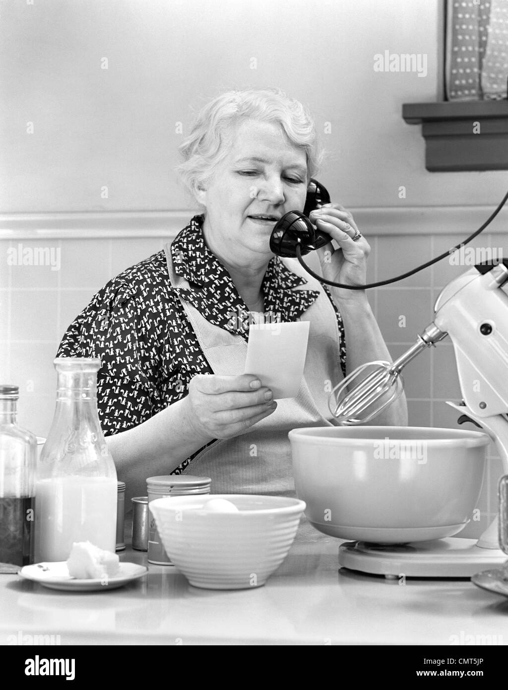 1940s donna nonna casalinga cuoco in cucina grembiule da indossare con frullatore ingredienti lettura elenco parlando al telefono Foto Stock