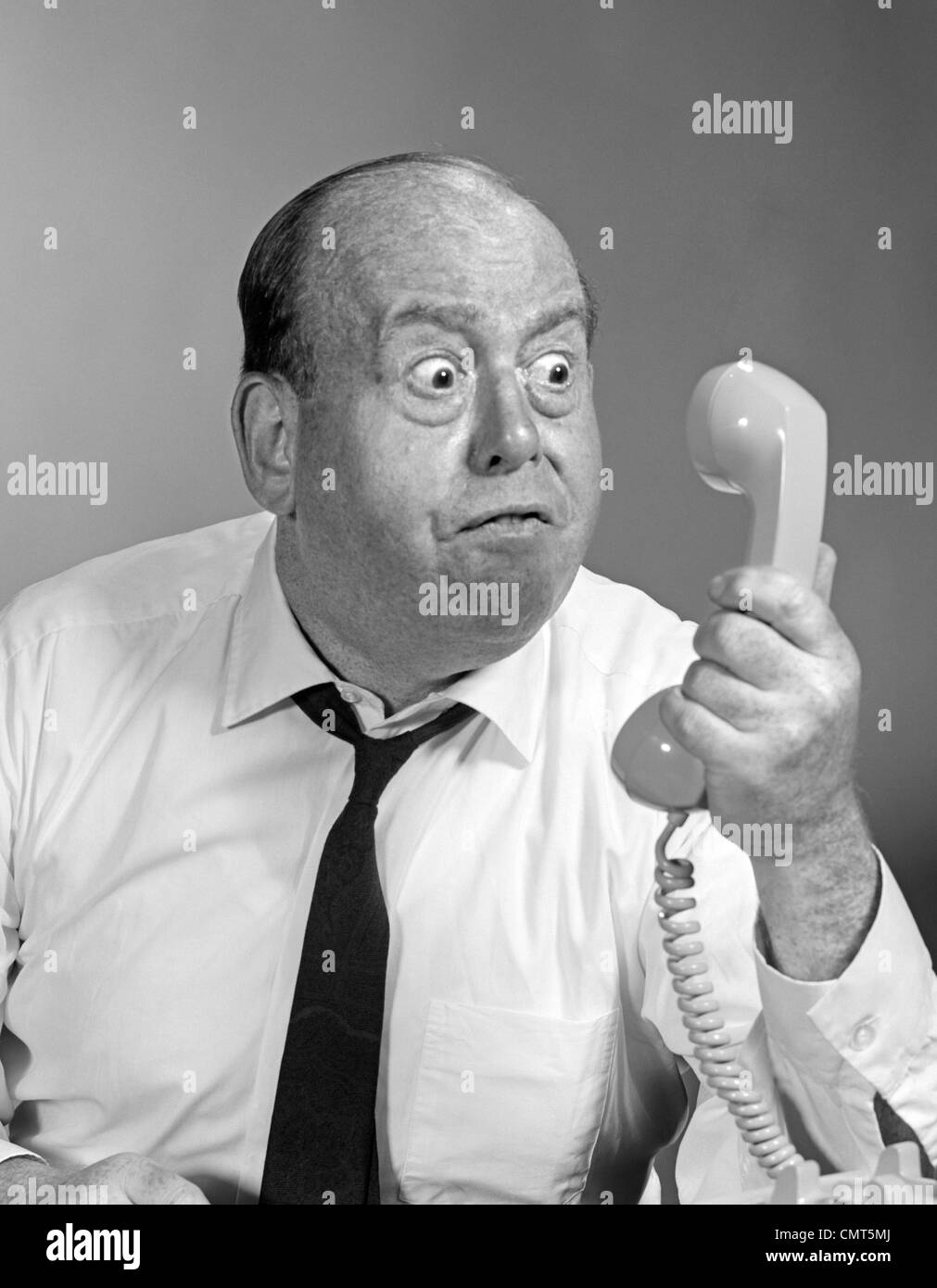 Anni sessanta anni settanta arrabbiato BALDING MAN LOOKING BUG-EYED nel ricevitore del telefono Foto Stock