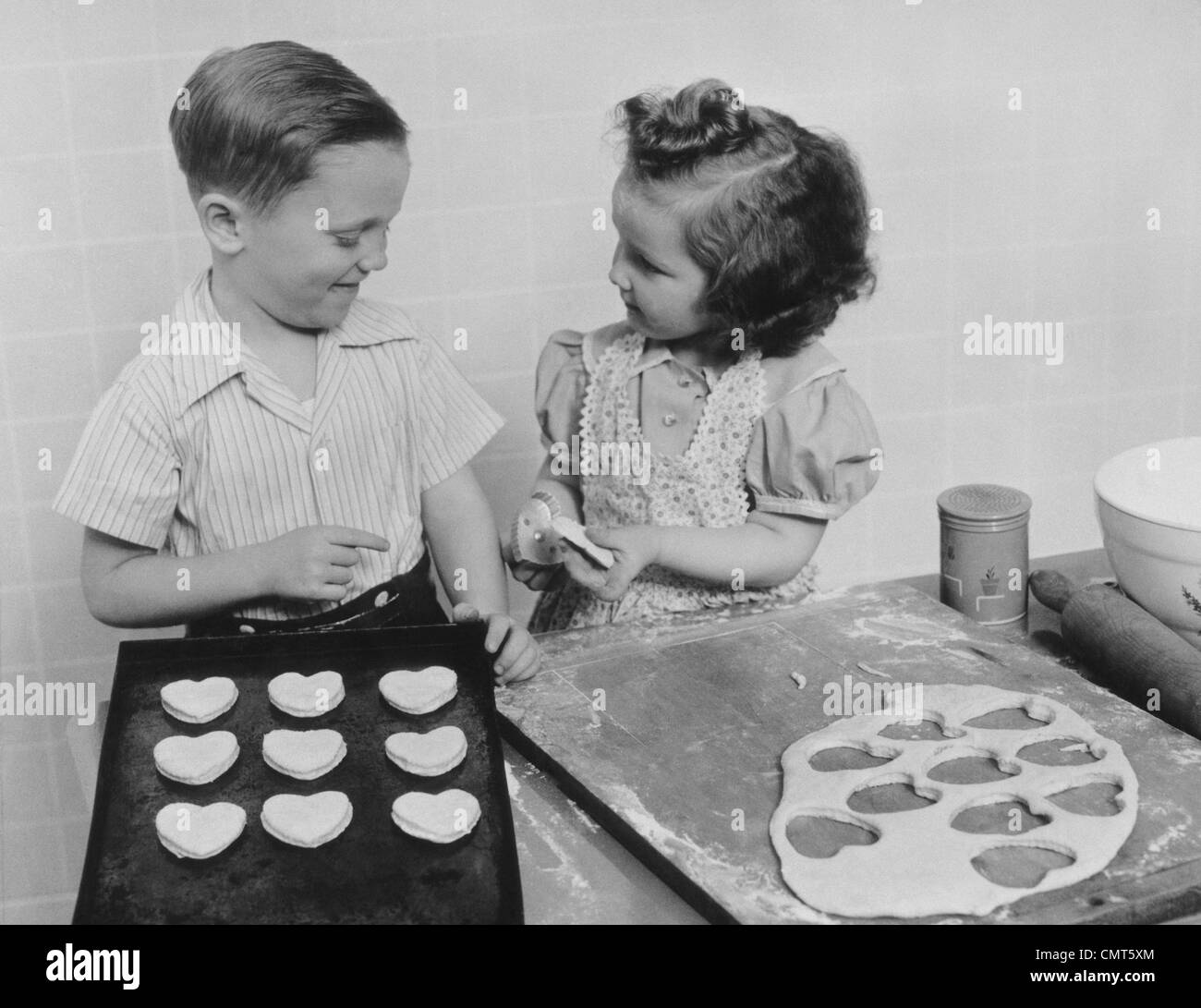 1940s giovane ragazza sorridente e ragazzo la cottura a forma di cuore i cookie di San Valentino Foto Stock