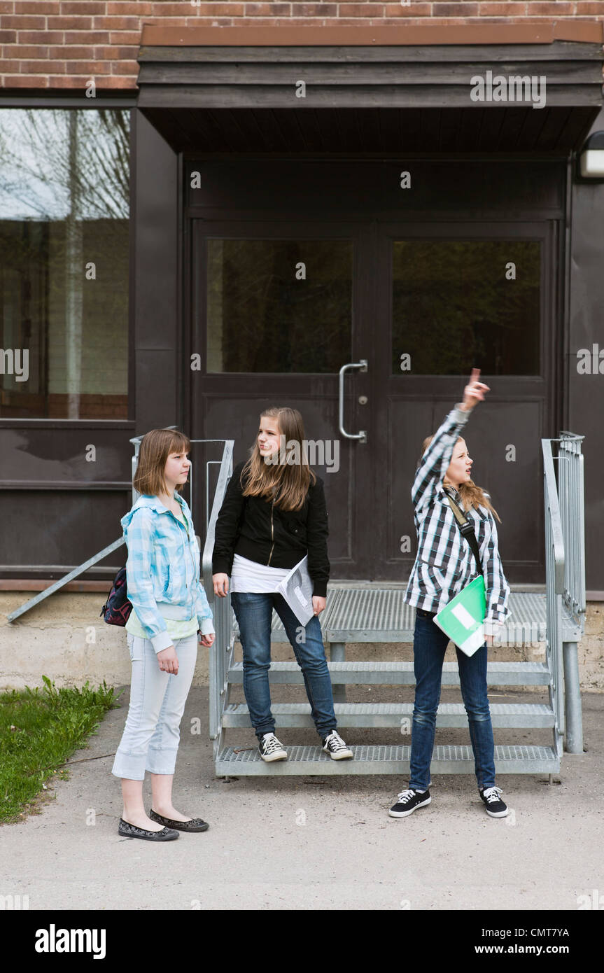 Lunghezza completa di tre amici (12-13) in attesa al di fuori della scuola Foto Stock