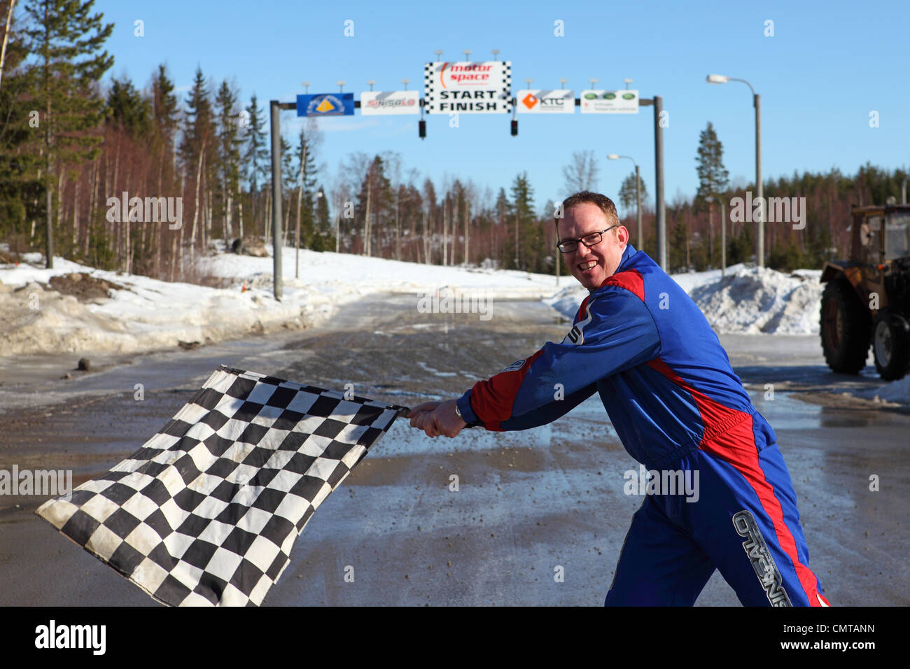 Un uomo in motorino-racing Tute sventola una bandiera a scacchi davanti a una data di inizio e di fine linea. Foto Stock