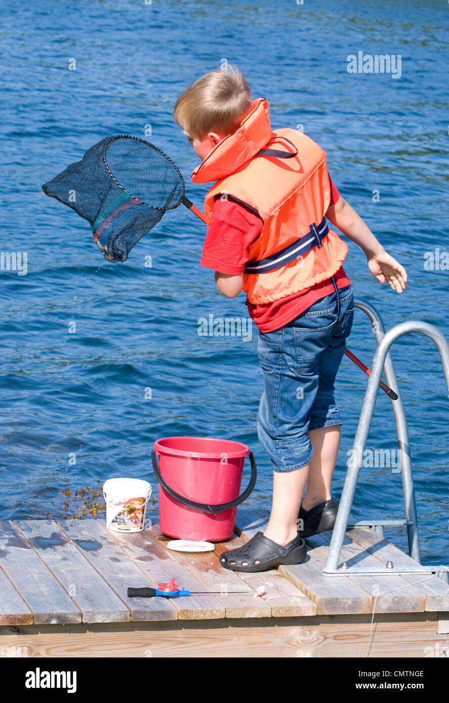 Ragazzo che indossa un giubbotto di salvataggio per la cattura di pesce con una landing net Foto Stock