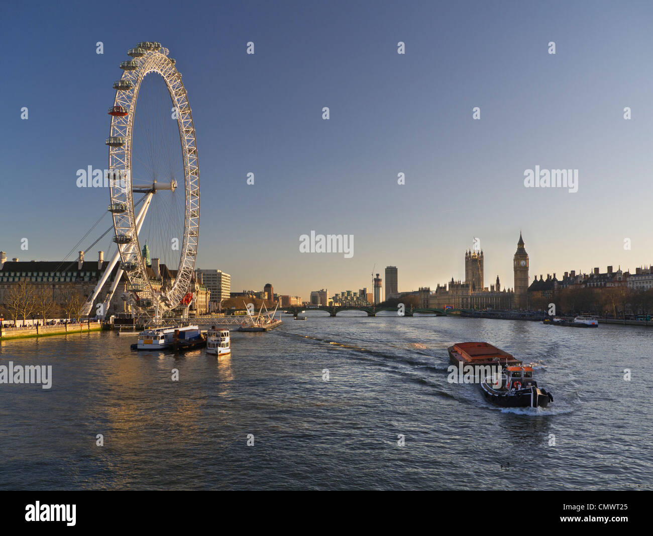 THAMES London Eye che tramonta il sole con chiatta fluviale funzionante che naviga a valle con Houses of Parliament vista di Londra paesaggio Regno Unito Foto Stock