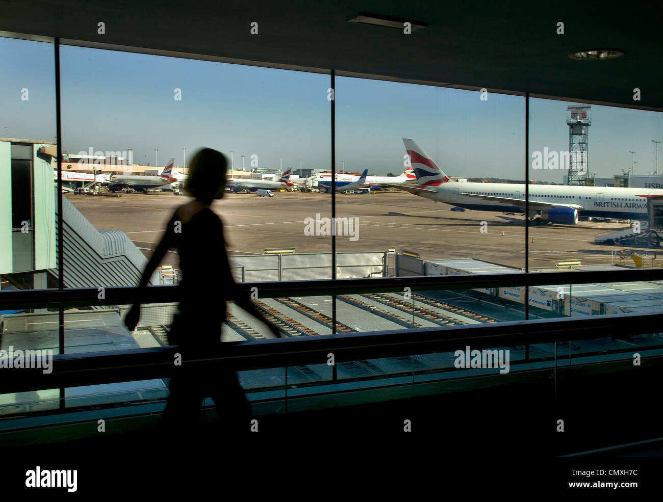 Donna oltrepassando la visualizzazione galleria all'aeroporto di Heathrow con British Airways aerei in background Foto Stock