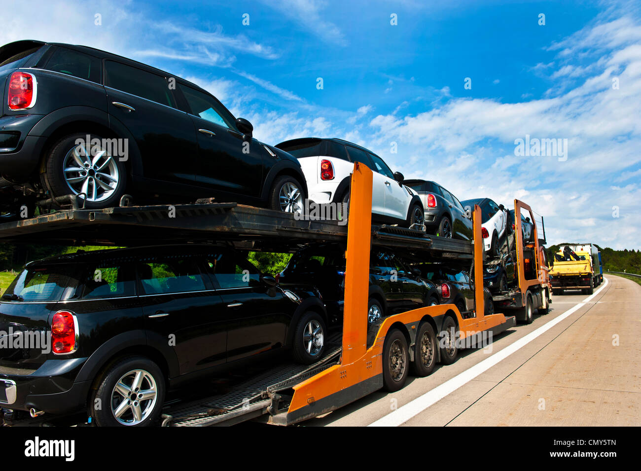 Un semi con una flotta di veicoli nuovi di marca in un giorno nuvoloso. Foto Stock