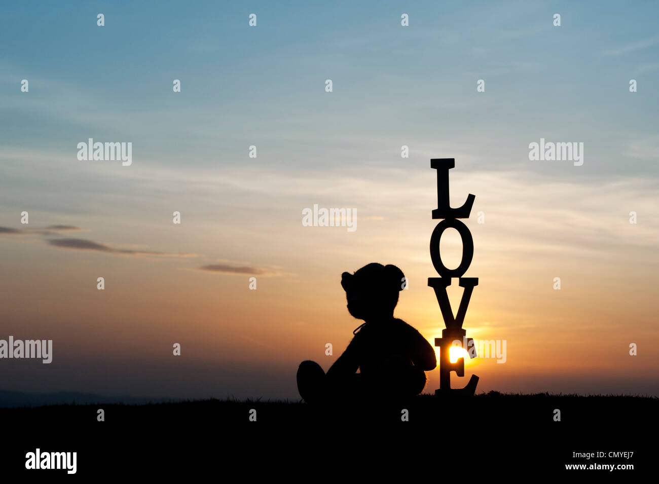 Orsacchiotto di peluche seduto accanto troppo la parola amore al tramonto. Silhouette Foto Stock