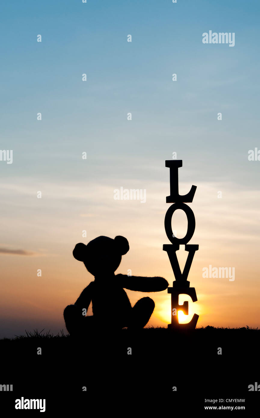Orsacchiotto di peluche seduto accanto troppo la parola amore al tramonto. Silhouette Foto Stock
