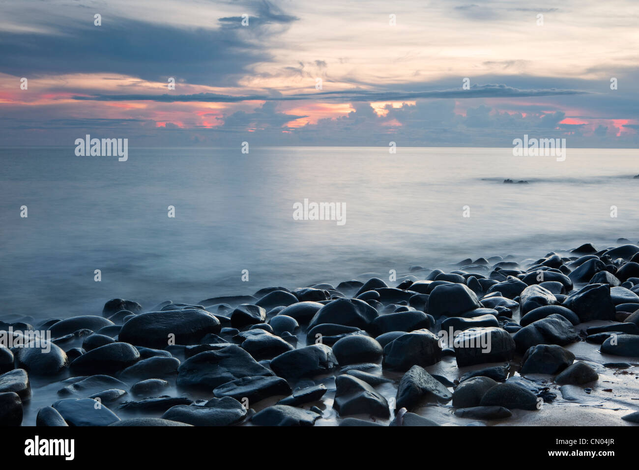 Onde che lambiscono le rocce in spiaggia con ciottoli all'alba, vicino a Cairns, Queensland, Australia Foto Stock