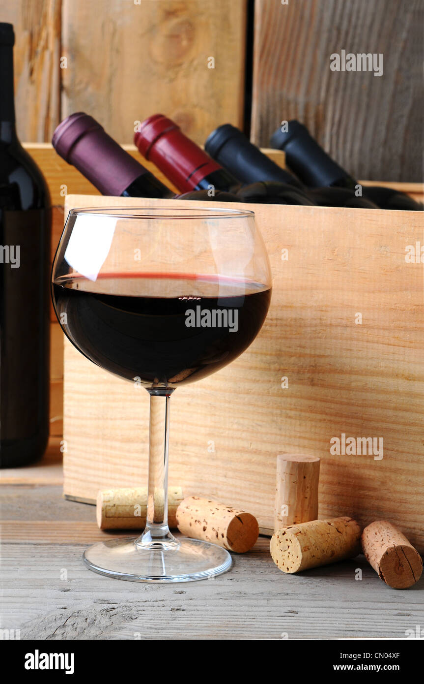Un bicchiere di vino rosso nella parte anteriore di una custodia in legno di bottiglie di vino su di un legno rustico sfondo. Formato verticale. Foto Stock