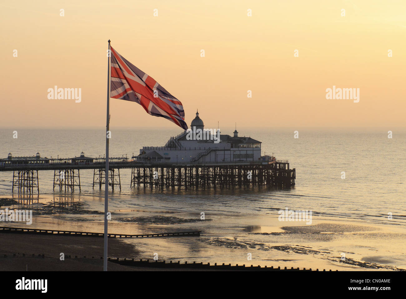 La britannica Union Jack flag battenti una bandiera pole con Eastbourne Pier in background, East Sussex, Inghilterra. Foto Stock