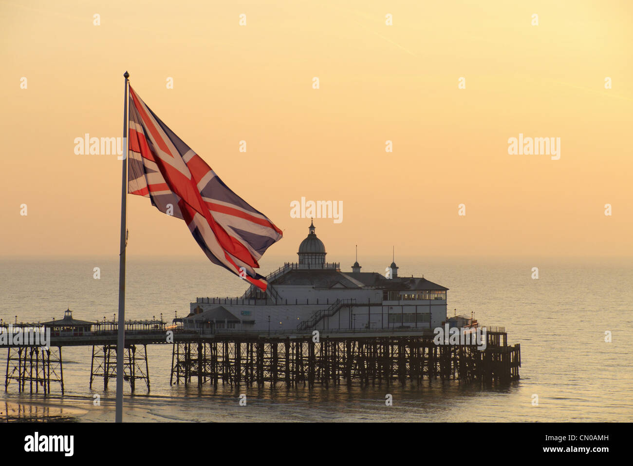 La britannica Union Jack flag battenti una bandiera pole con Eastbourne Pier in background, East Sussex, Inghilterra. Foto Stock