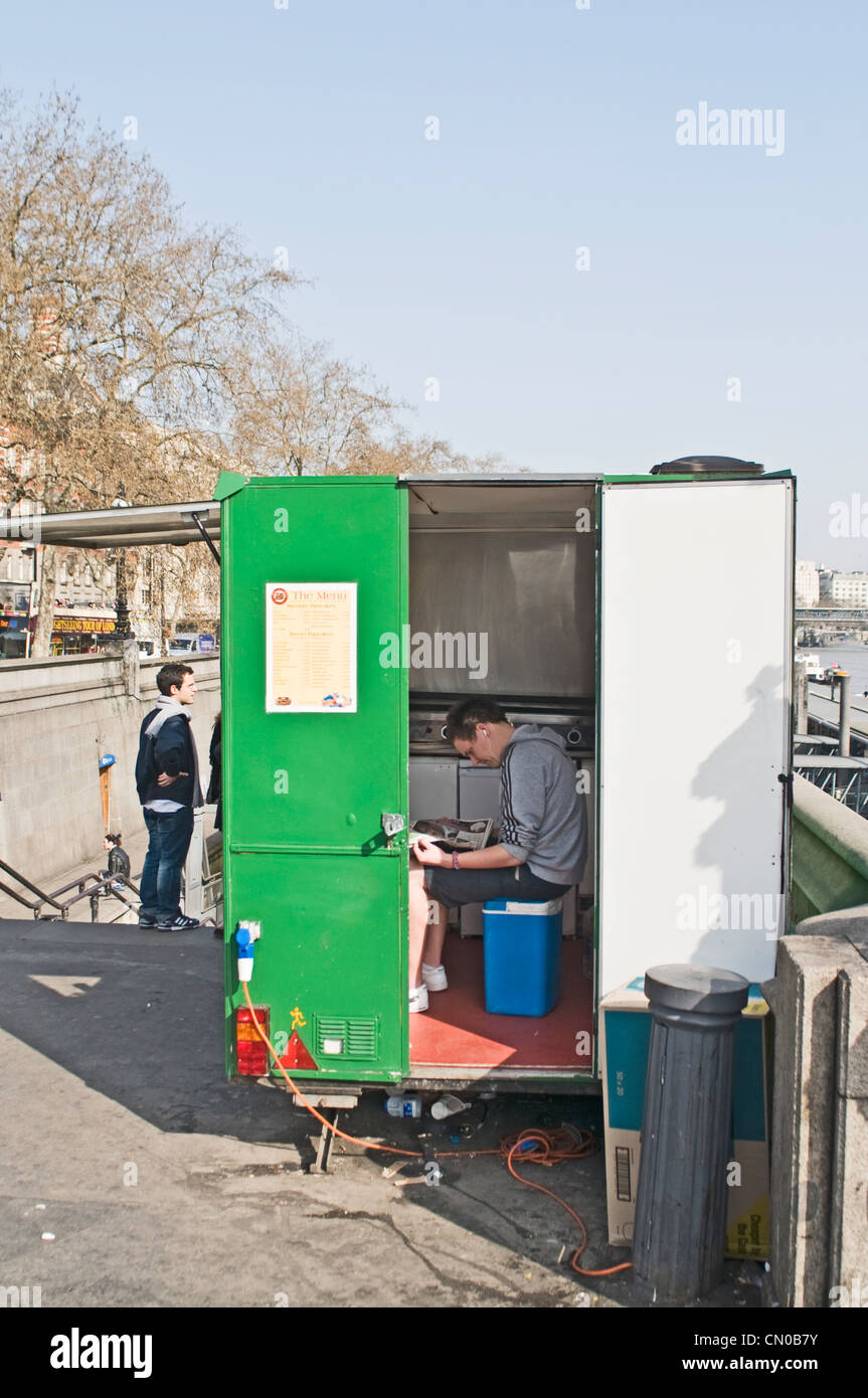 Un uomo che legge il suo giornale in un burger van Foto Stock