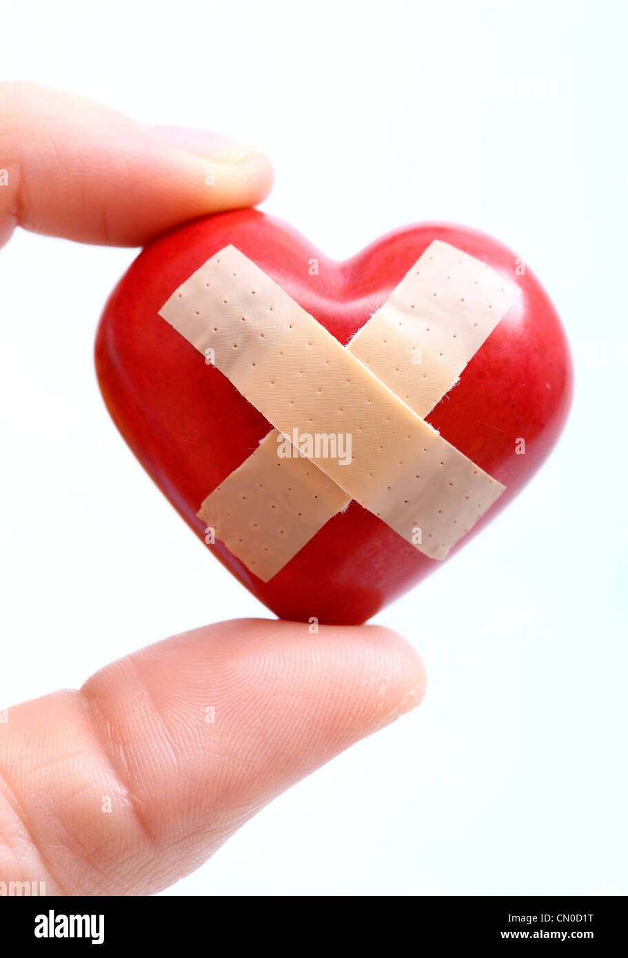 Immagine simbolica, malattie cardiache, infarto, protezione, prevenzione, cardiologia. Mani tenendo un cuore rosso con una banda-aiuto. Foto Stock