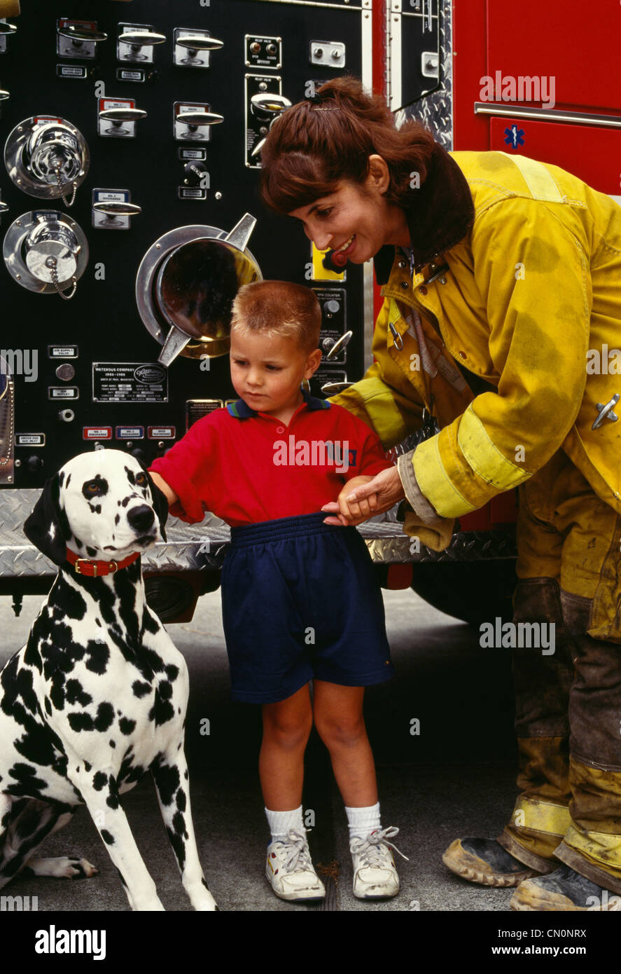Donna pompiere aiuta le piccole boy a pet firehouse dog. Foto Stock