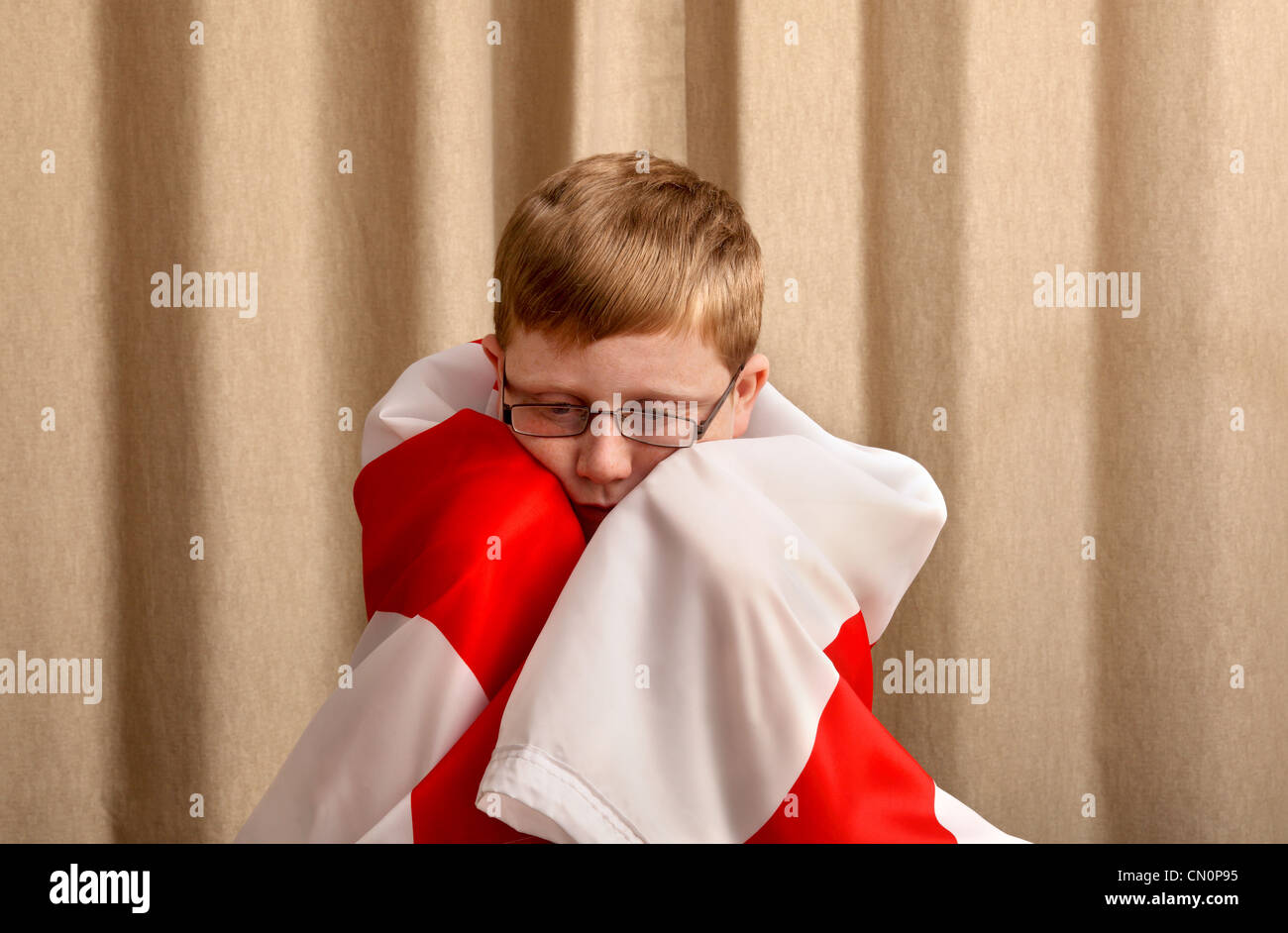 Un triste guardando 12 anno vecchio ragazzo con l'Inghilterra bandiera drappeggiato attorno alle sue spalle Foto Stock
