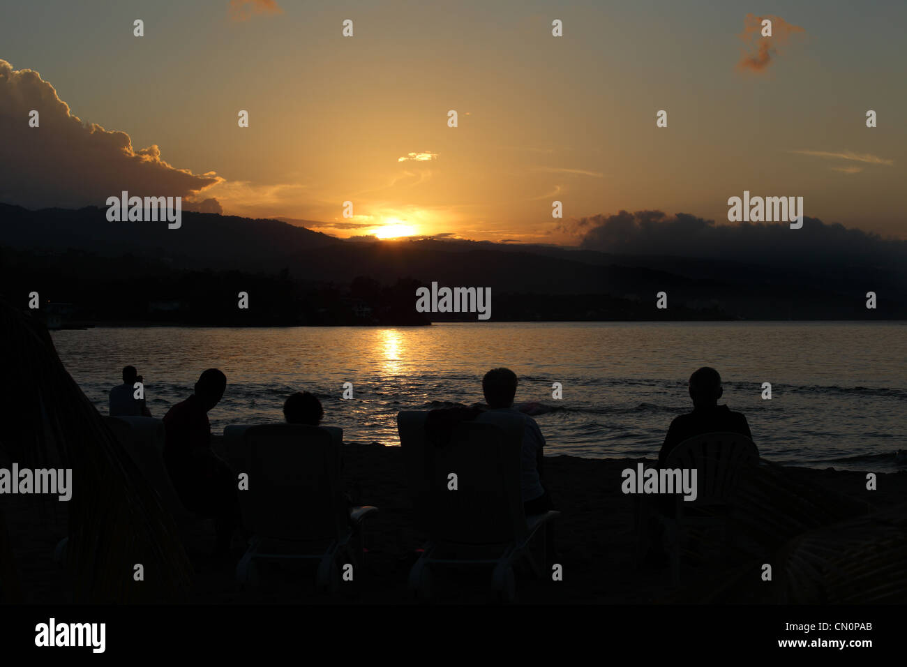Vacanzieri relax su una spiaggia a guardare il tramonto a Sans Souci, Giamaica Foto Stock
