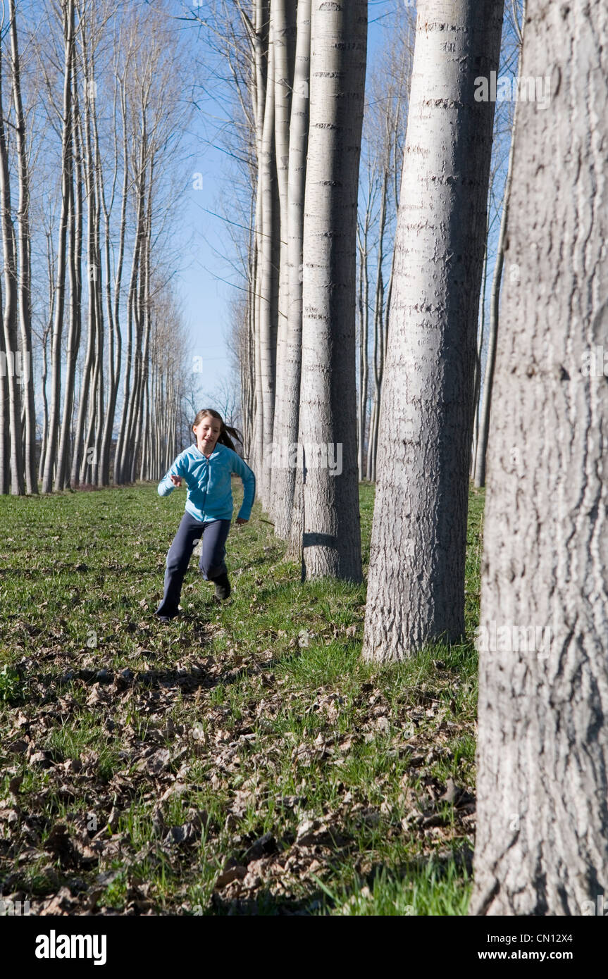 Giovane ragazza che corrono tra gli alti alberi Foto Stock