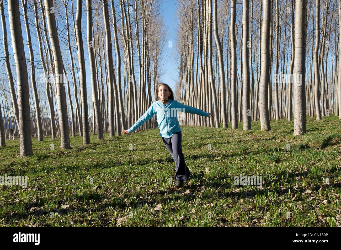 Giovane ragazza che corrono tra gli alti alberi Foto Stock