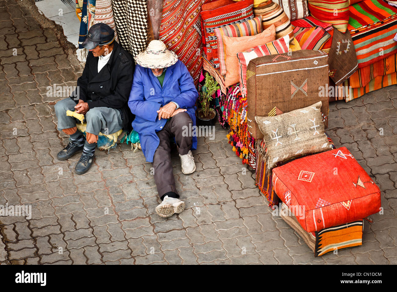 Due uomini in appoggio su una pila di tappeti nel Souk, Medina, Marrakech, Marocco Foto Stock