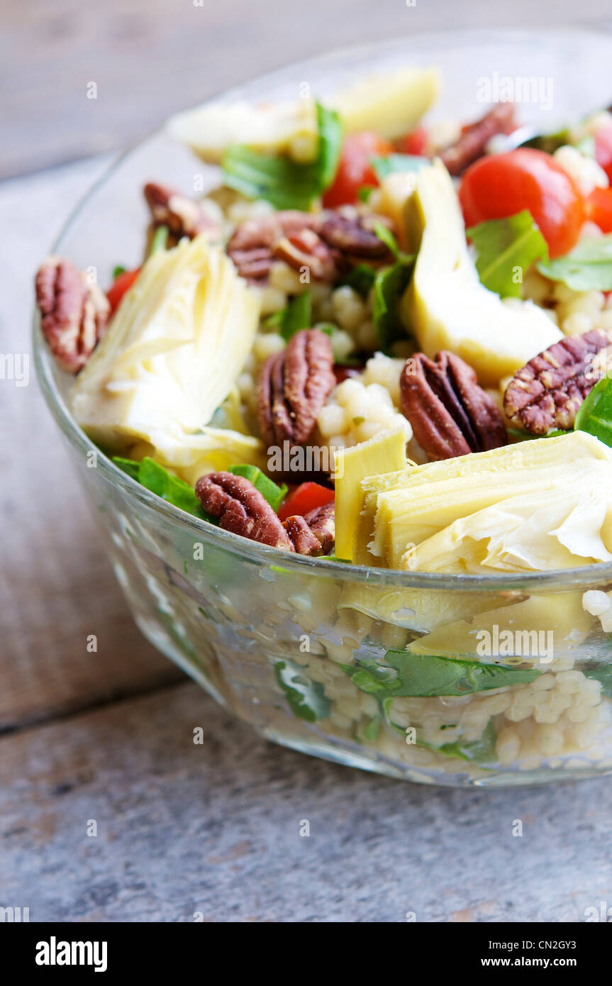 Una rinfrescante insalata con cuori di carciofo, grandi cuscus, argula foglie, pomodorini e noci pecan tostate e. Foto Stock
