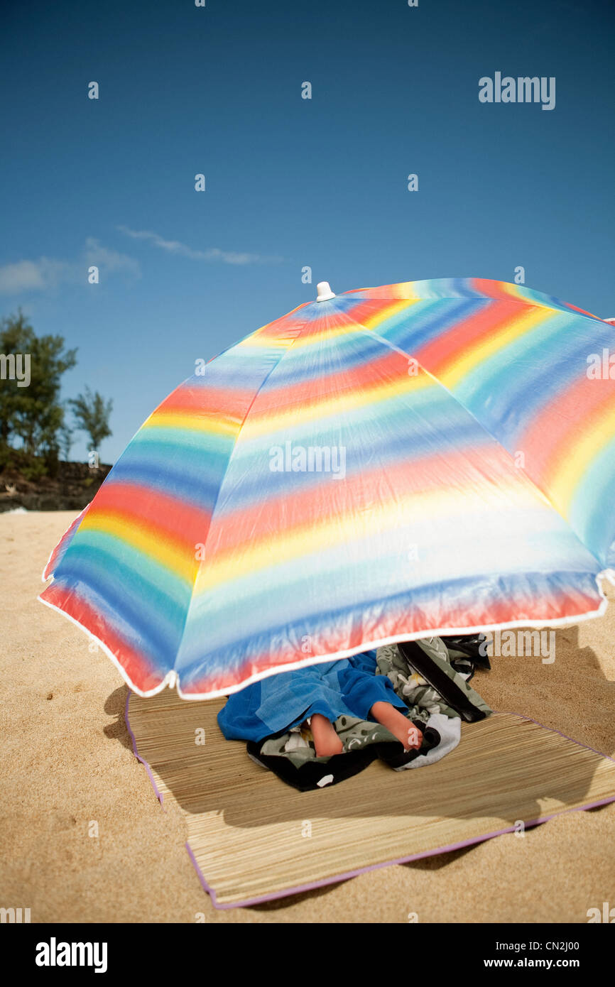 Ragazzo che giace sotto ombrellone sulla spiaggia sabbiosa Foto Stock