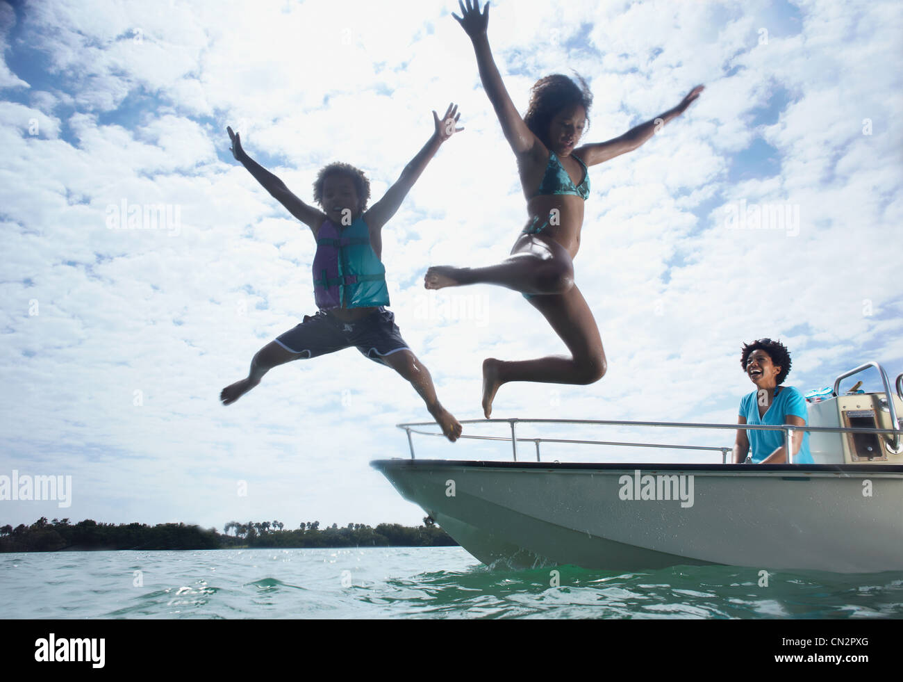 Madre di motoscafo, due bambini saltando in acqua Foto Stock