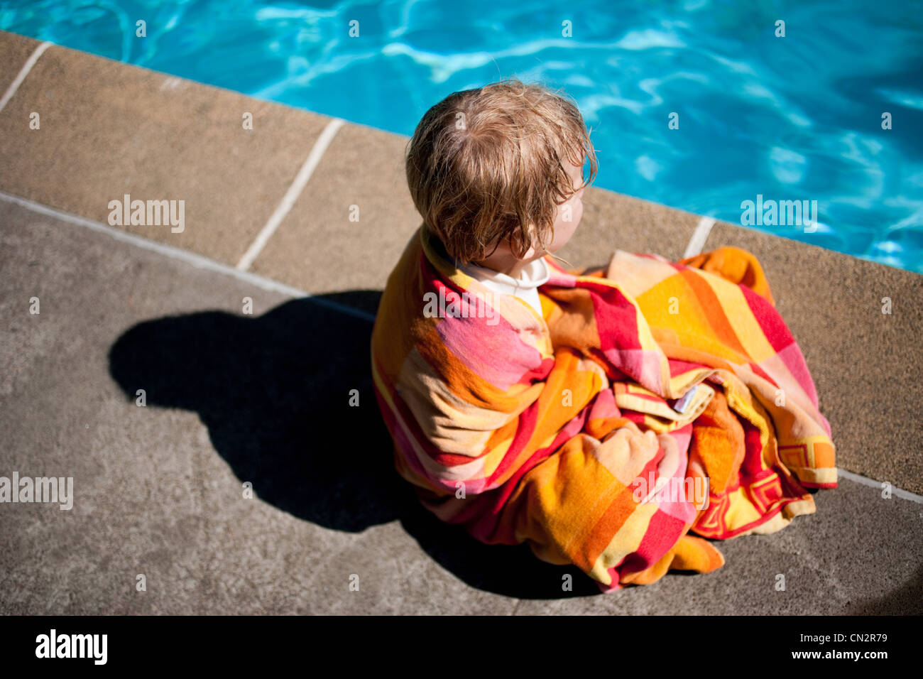 Ragazzo seduto a bordo piscina avvolto in asciugamano Foto Stock