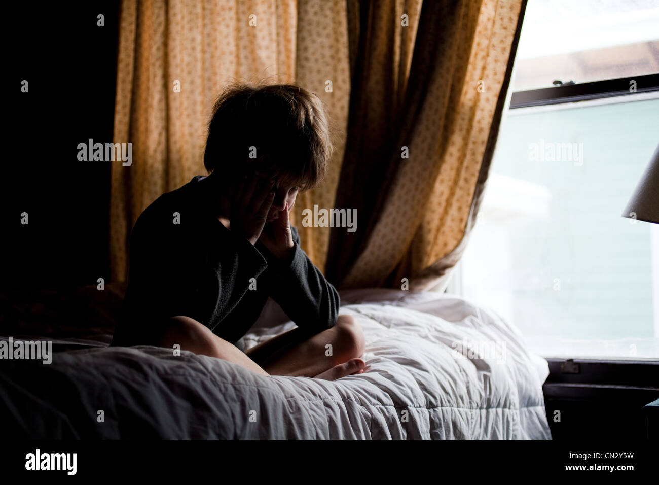 Ragazzo seduto sul letto a piangere Foto Stock