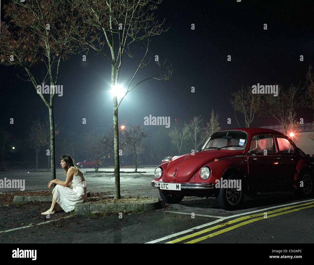 Donna seduta nel parco auto di notte Foto Stock