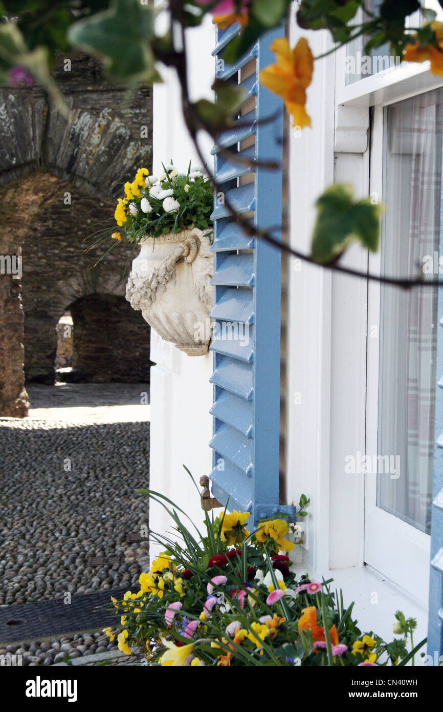 Il francese otturatore della finestra accanto alla finestra sul vecchio cottage accanto alla strada di ciottoli con fiori. Foto Stock