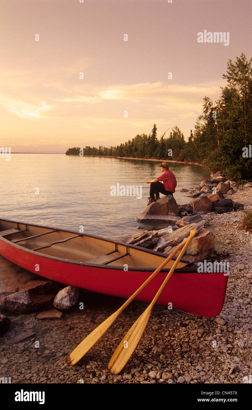 Giovane uomo relax su una roccia nei pressi di una canoa, piccolo lago di calcare, Manitoba Foto Stock