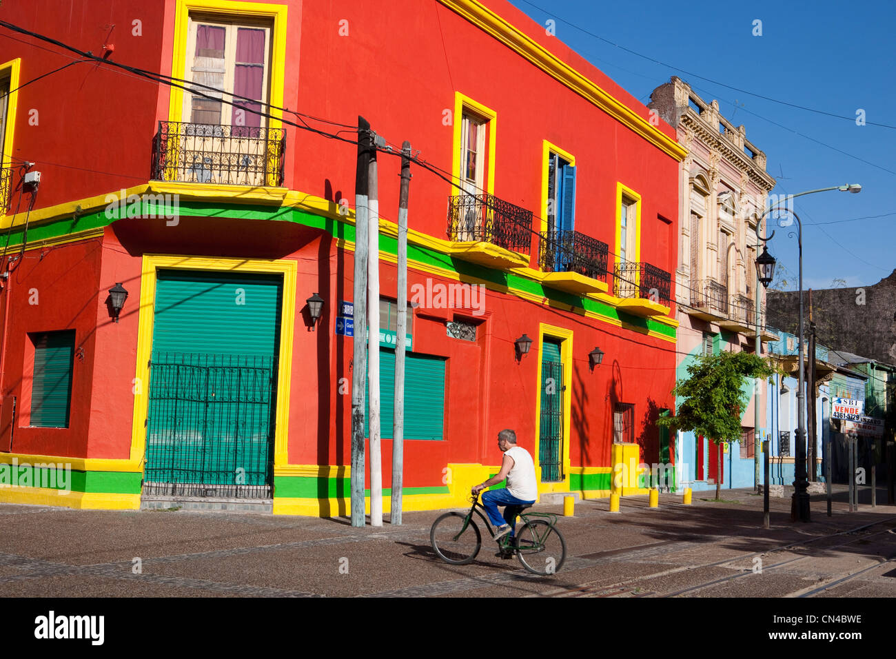 Argentina, Buenos Aires, La Boca distretto, uomo ciclismo su strada Garibaldi nei pressi di Caminito street e edificio colorato Foto Stock