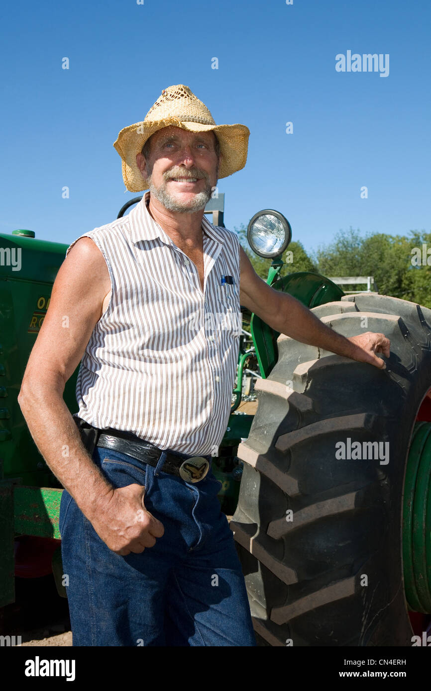 Senior agricoltore appoggiata contro il trattore, sorridente Foto Stock