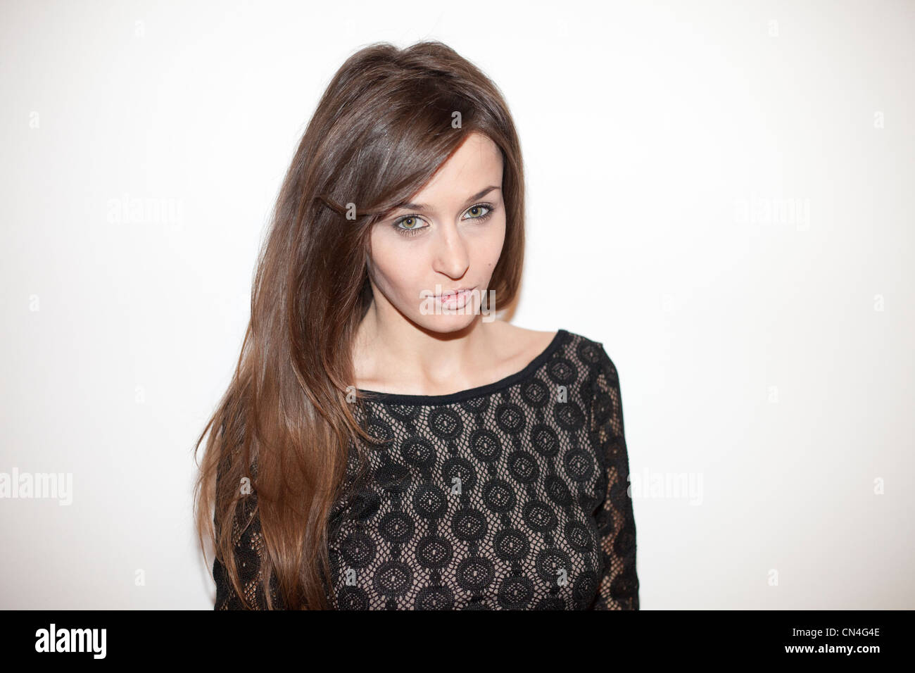 Giovane donna sicura di sé con lunghi capelli marroni che posa con le mani sui fianchi, con un top in pizzo nero, su uno sfondo bianco Foto Stock