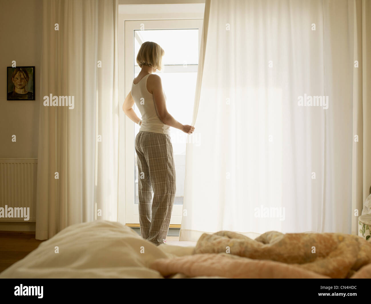 Donna matura indossando pigiami di apertura tende camera da letto Foto Stock