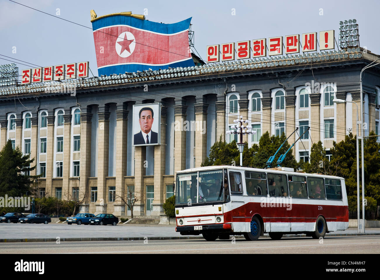 Corea del Nord Pyongyang, Kim Il-Sung square, filobus guidando attraverso un ritratto di Kim Il-Sung appeso sulla facciata del Foto Stock