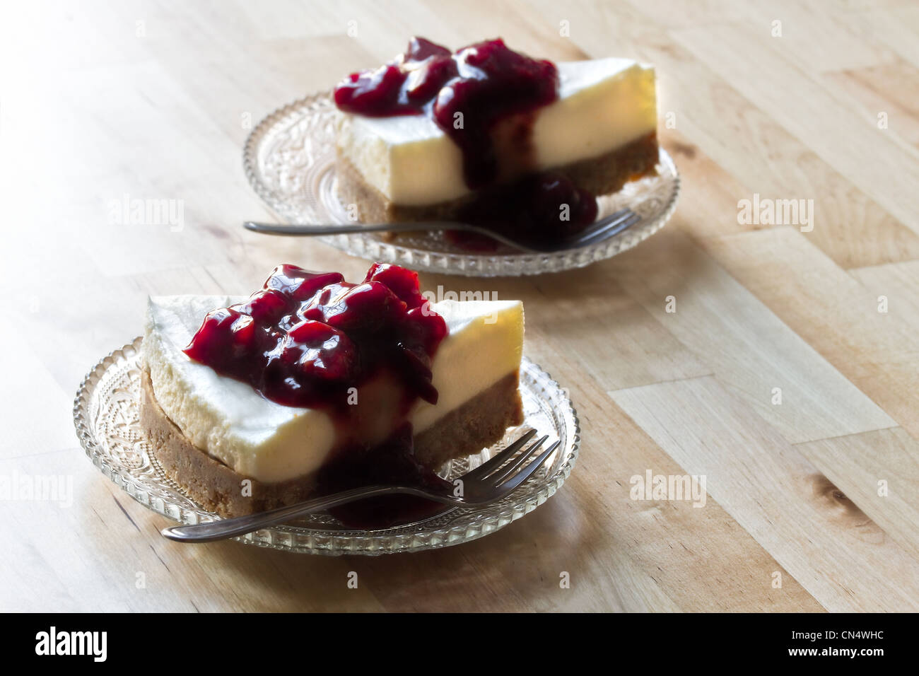 Tavolo in legno con due pezzi Mon Chou tart decorate con salsa alle ciliegie su piattini di vetro - immagine orizzontale Foto Stock